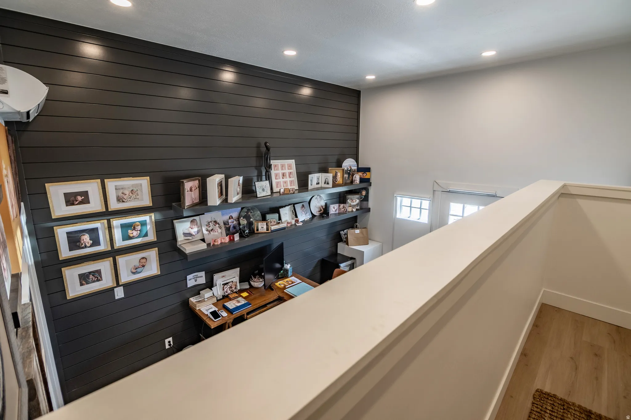 Recessed lighting, wood-finish flooring, half wall railing, painted horizontal plank wall, built-in shelving