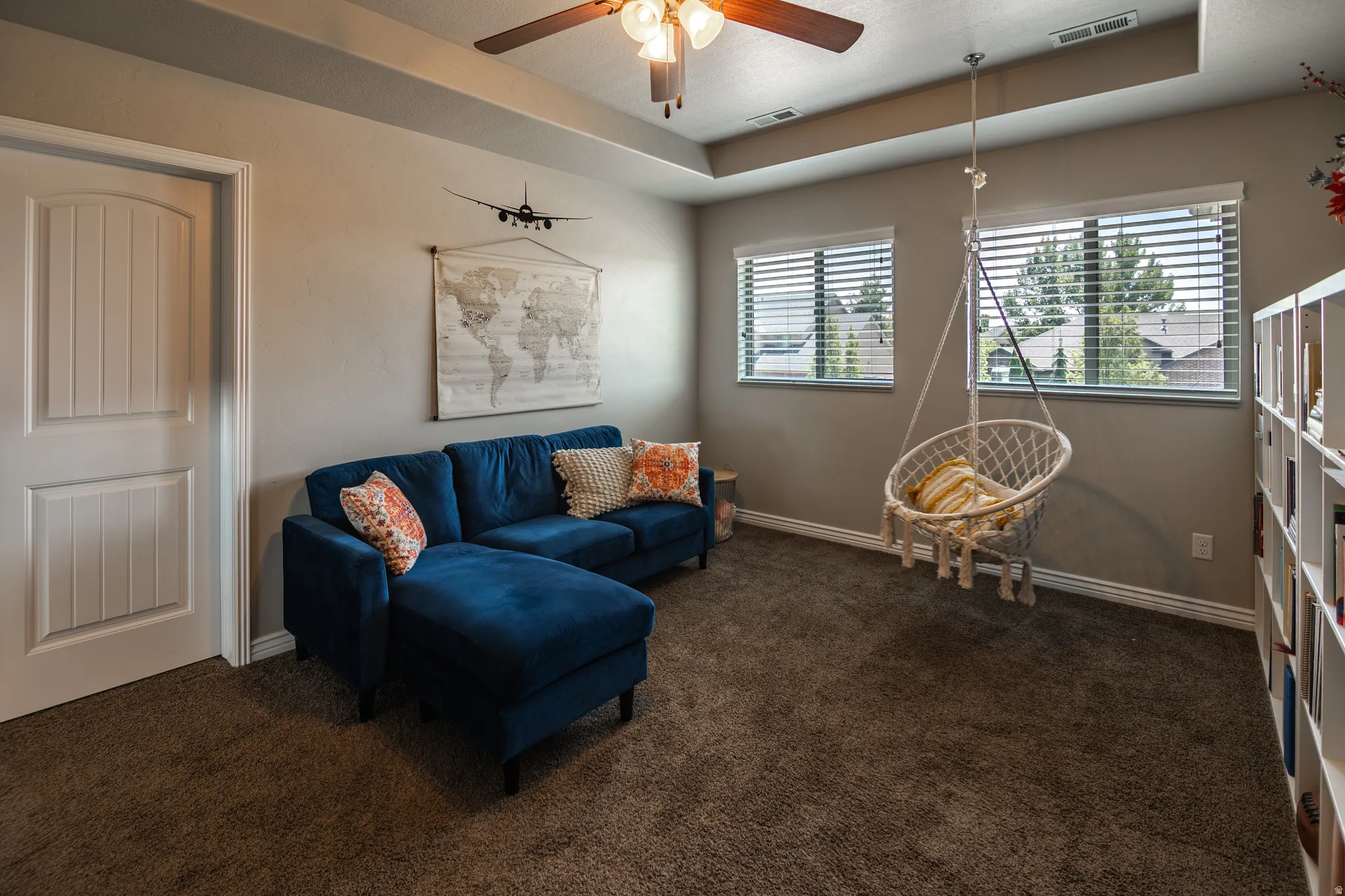 Tray ceiling with a ceiling fan, two windows with blinds, and carpeted flooring