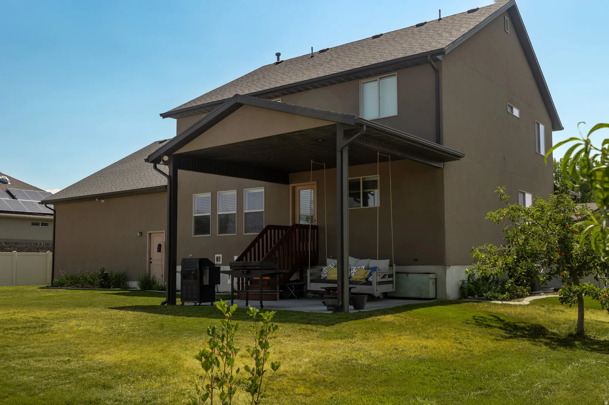 Expansive grassy yard with mature trees, a covered patio, and a wood deck with stairs
