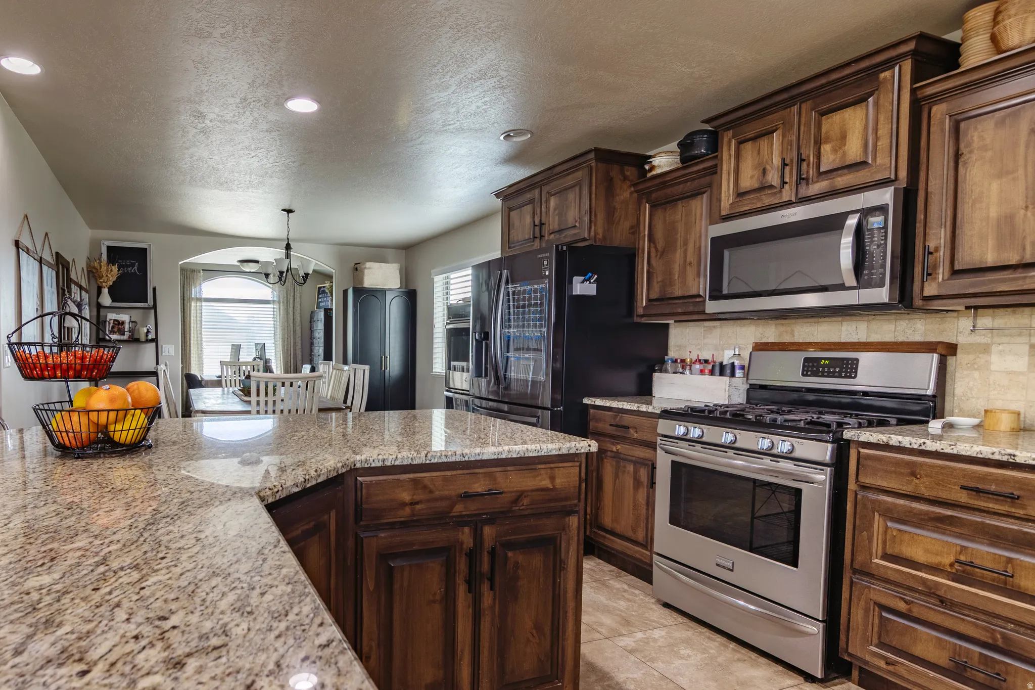 Kitchen featuring wood-finish cabinetry, stainless steel appliances, granite countertops, and tile flooring