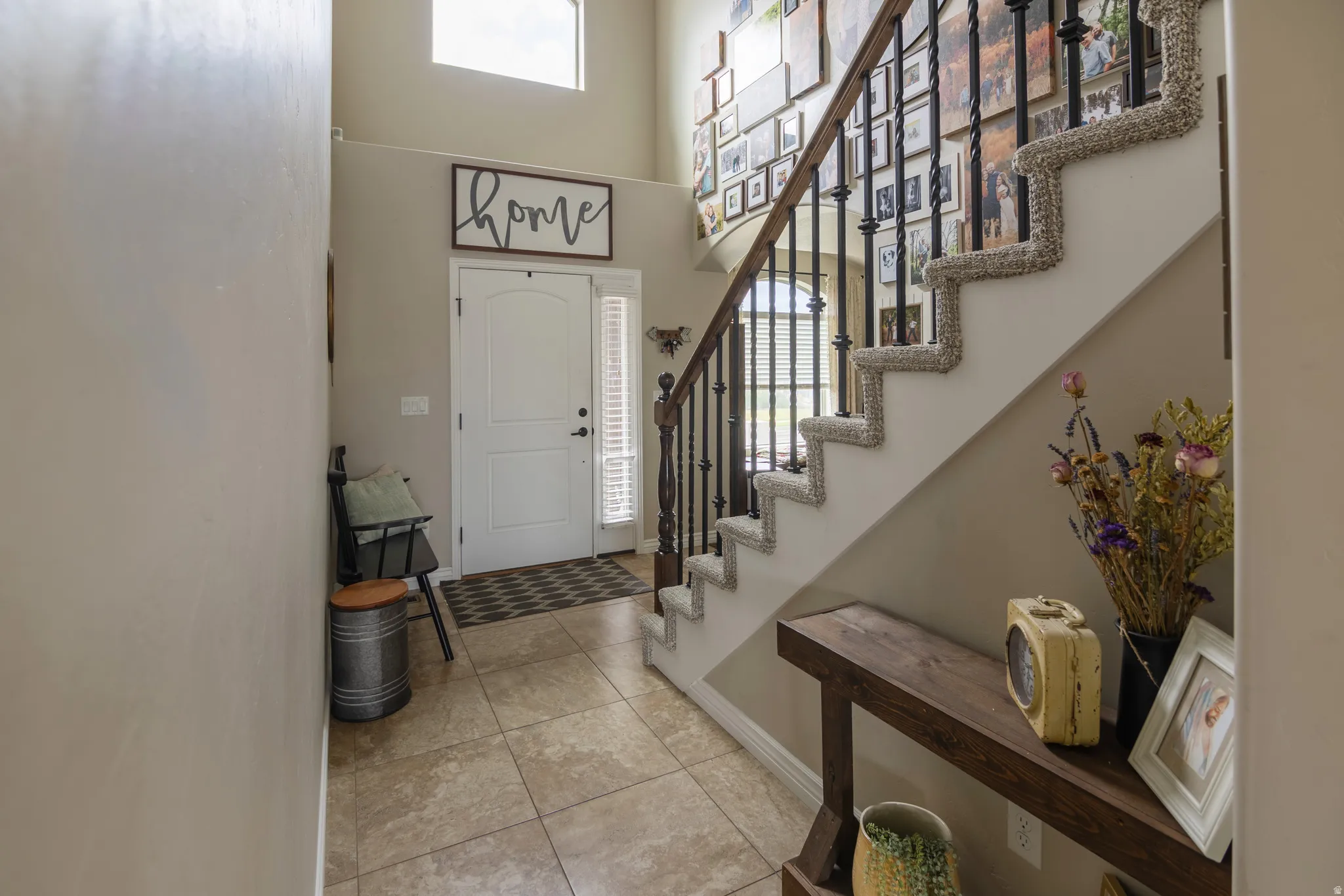Foyer with high ceilings, transom window, tile flooring, and a staircase featuring wrought iron balusters