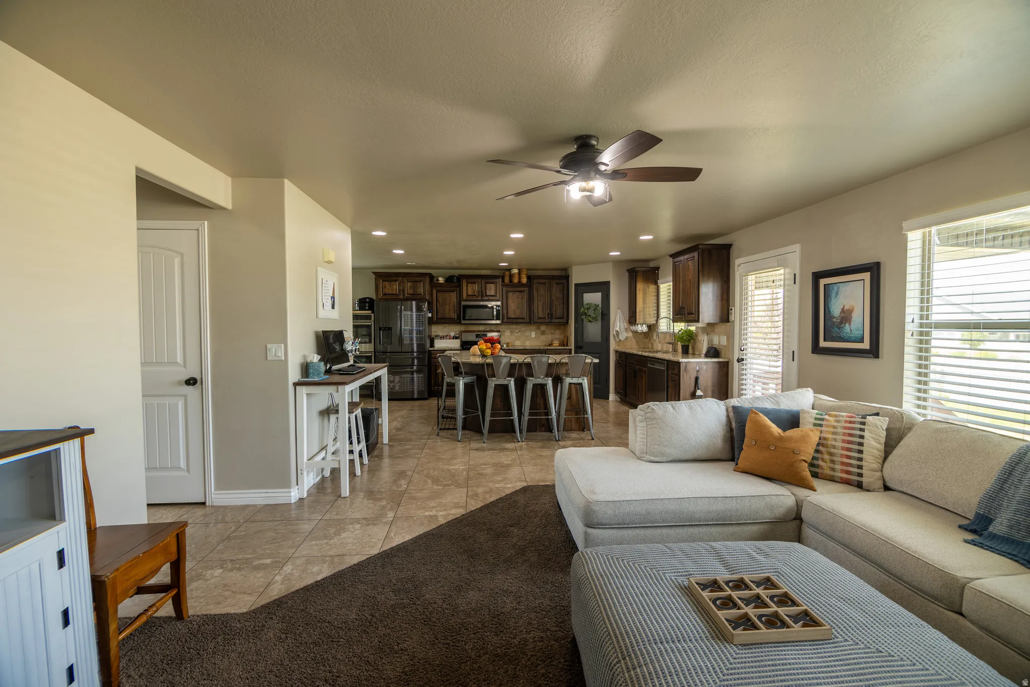Open concept living space featuring a ceiling fan, tiled flooring, dark wood cabinetry, a kitchen island with seating, and recessed lighting