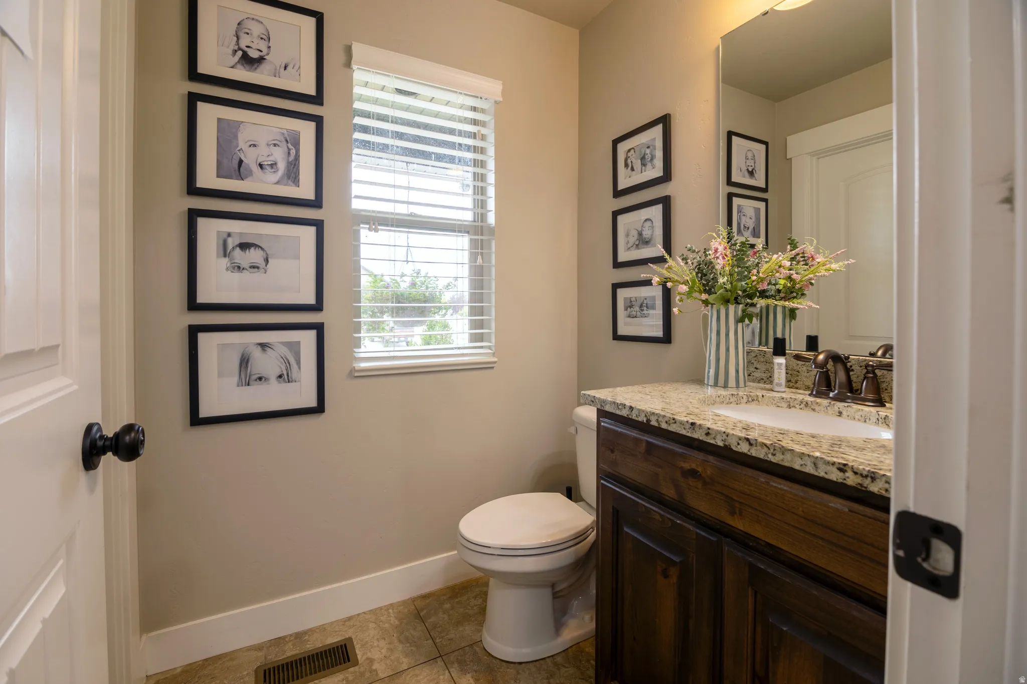 Powder room featuring a wood-finish vanity with a stone countertop, an undermount sink, and tiled flooring