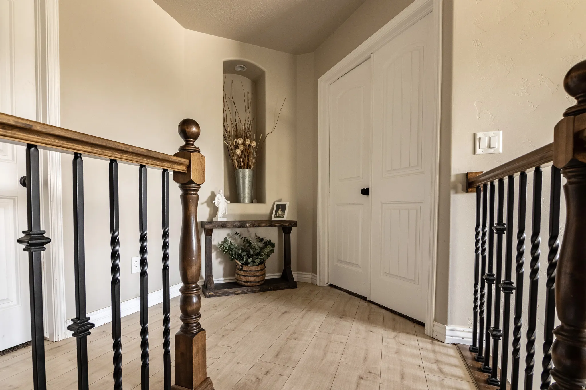 Wood-finish flooring, recessed wall niche, paneled bifold doors, and a wood and wrought iron staircase