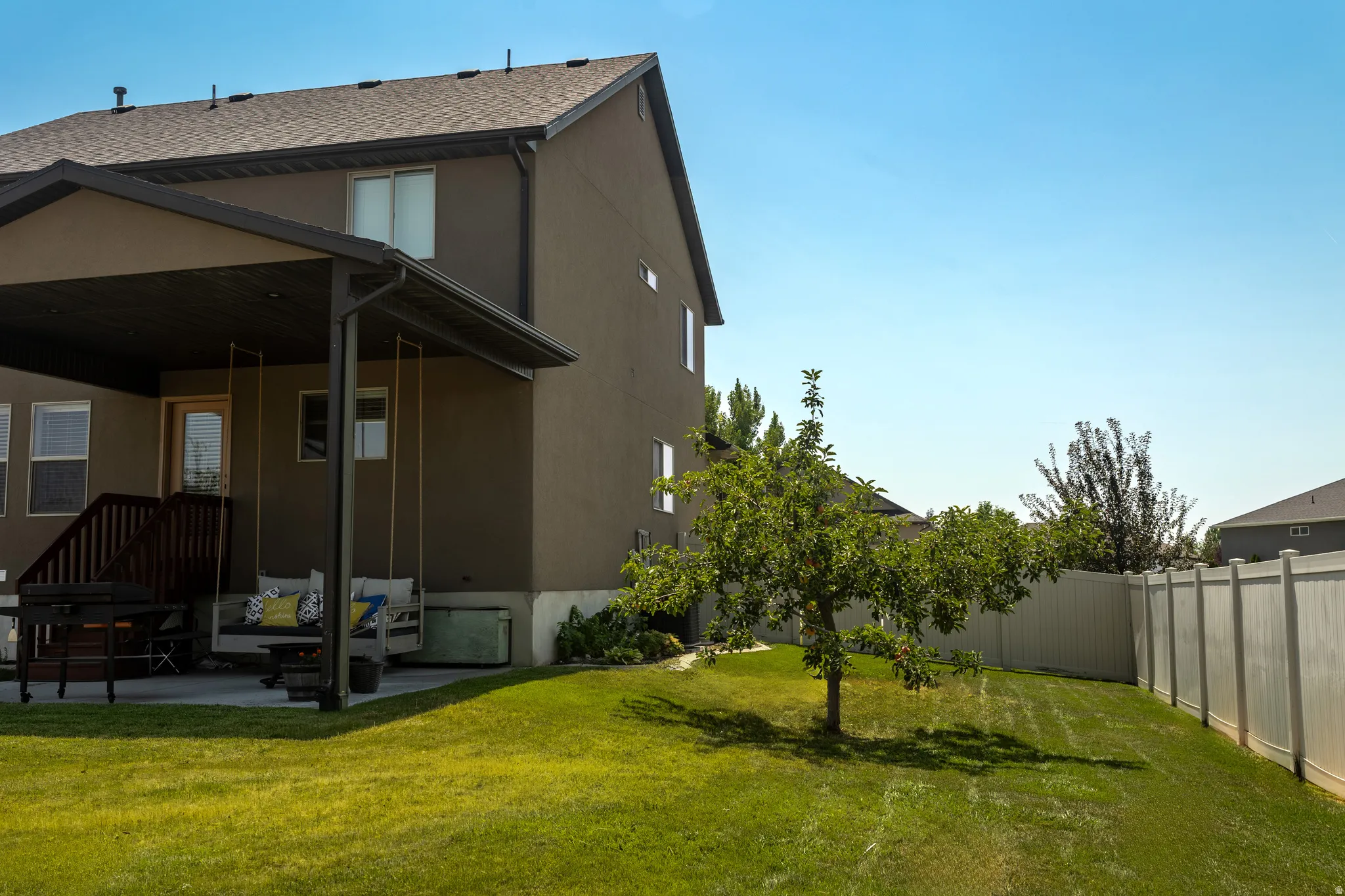 Expansive backyard with a covered patio, concrete surface, and a manicured lawn featuring a fruit tree