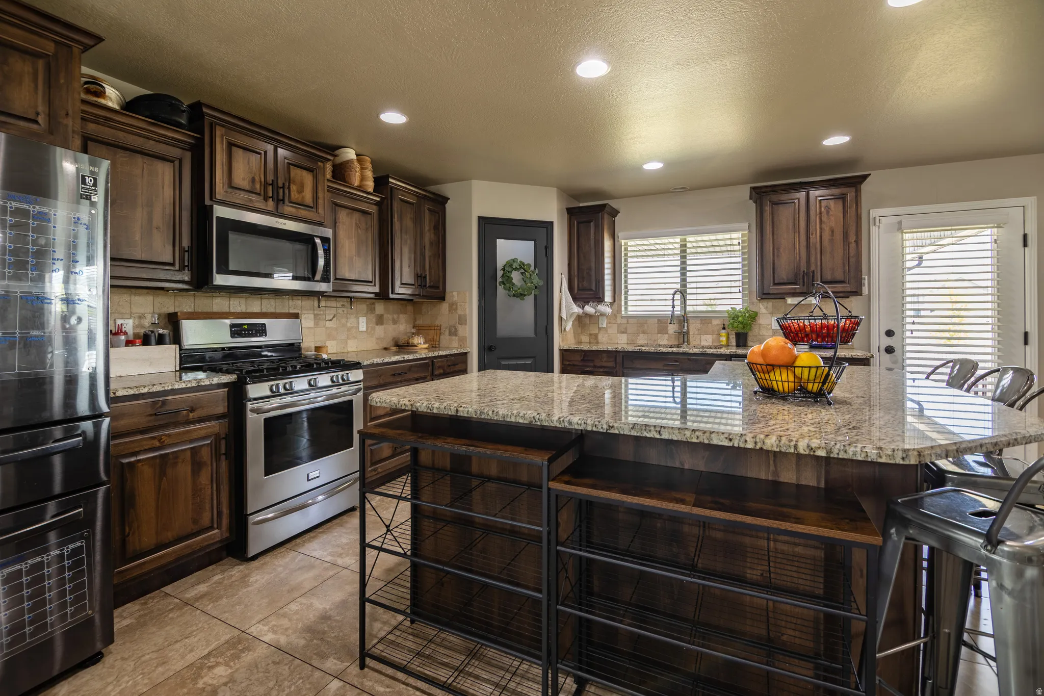 Kitchen featuring a large island with stone-finish countertop, stainless steel appliances, wood-finish cabinetry, and recessed lighting