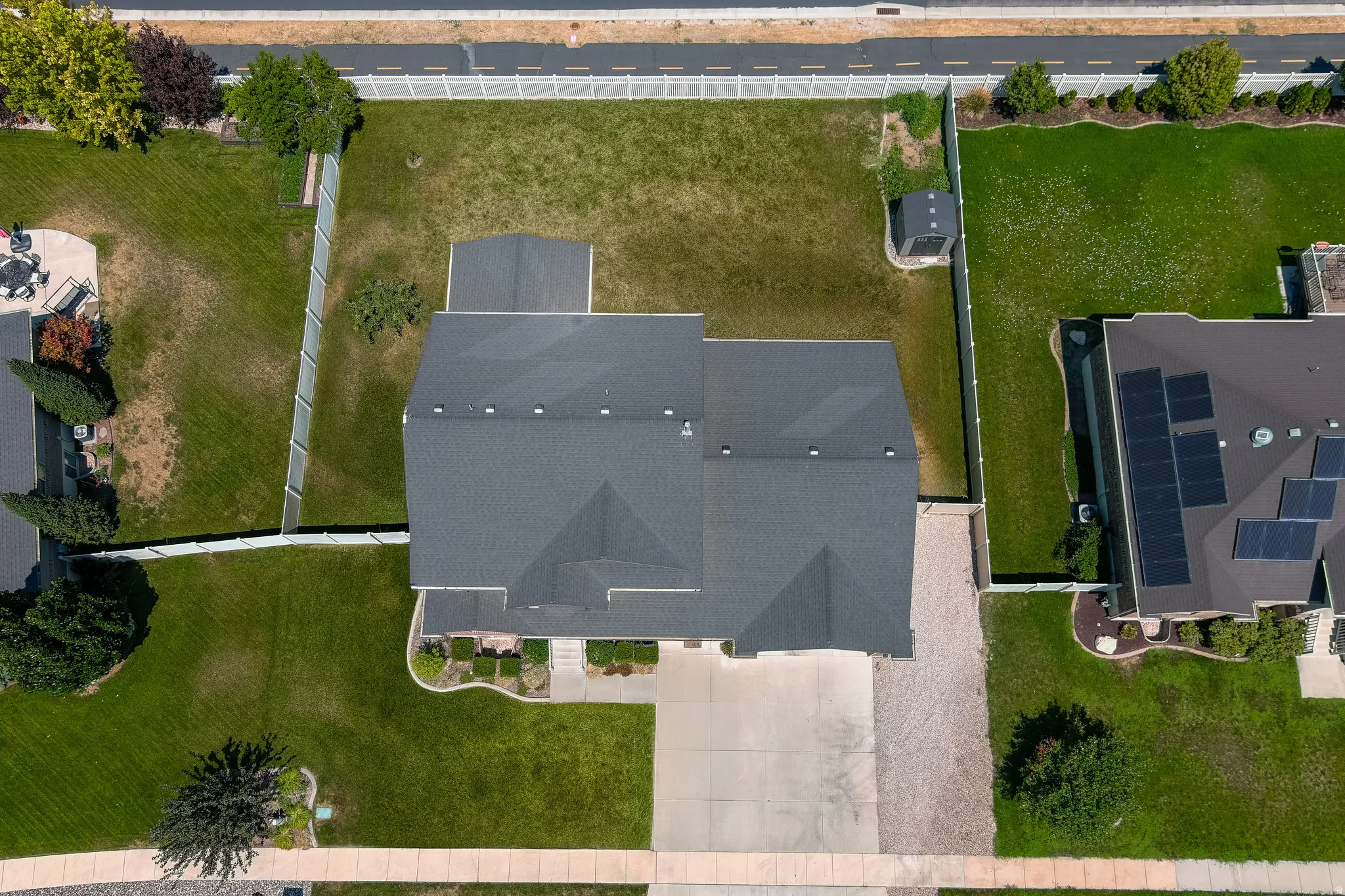 Expansive lot with lush green lawn, mature trees, concrete driveway, and a fenced perimeter