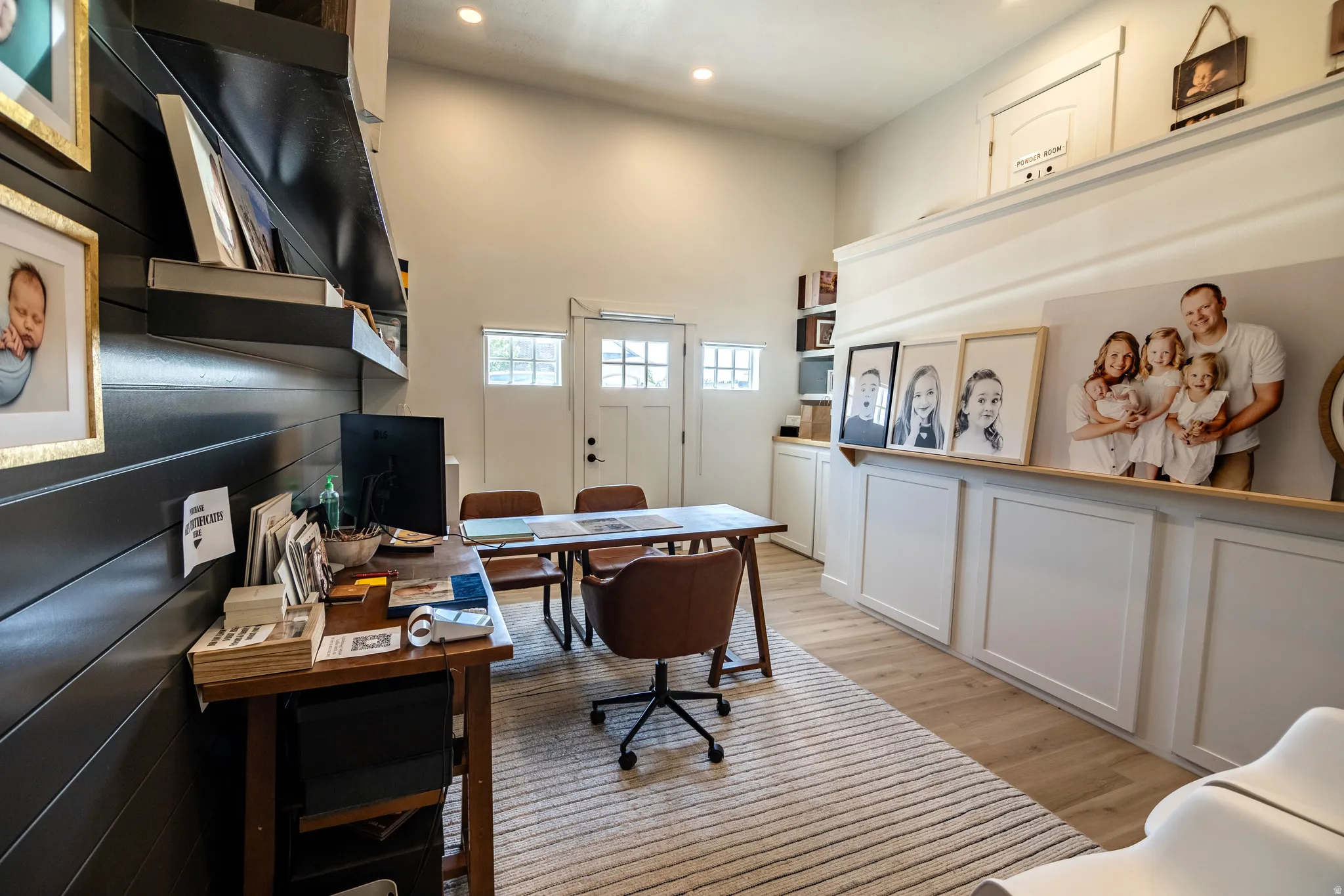 Vaulted ceilings with recessed lighting, light wood-finish flooring, white paneled lower cabinetry, white shaker-style door, and black shiplap accent wall