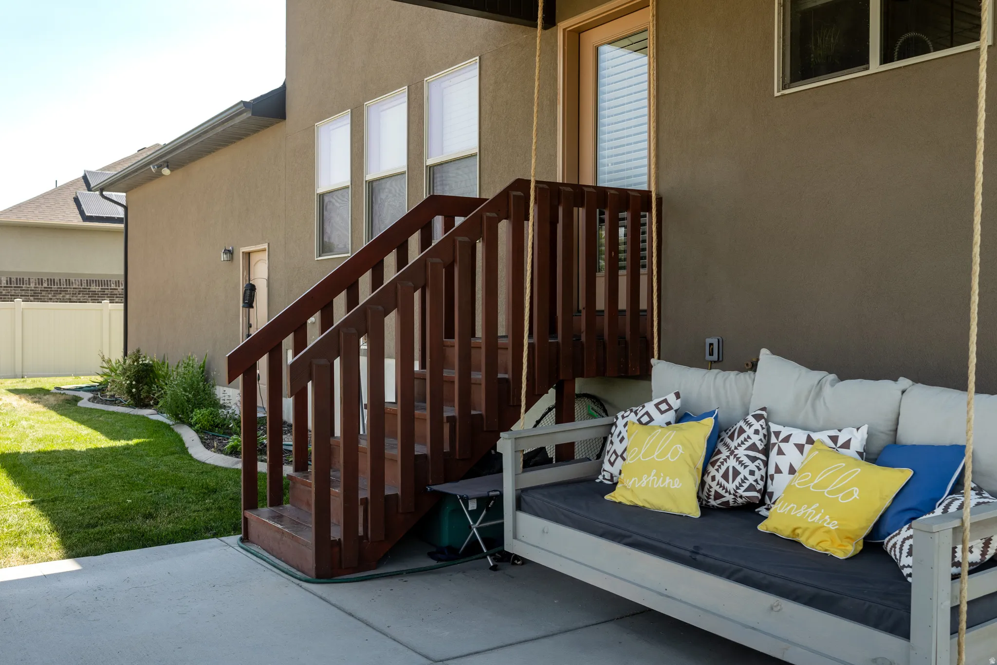 Concrete patio featuring a wood-stained staircase with railing, stucco exterior, and a manicured lawn with garden bed