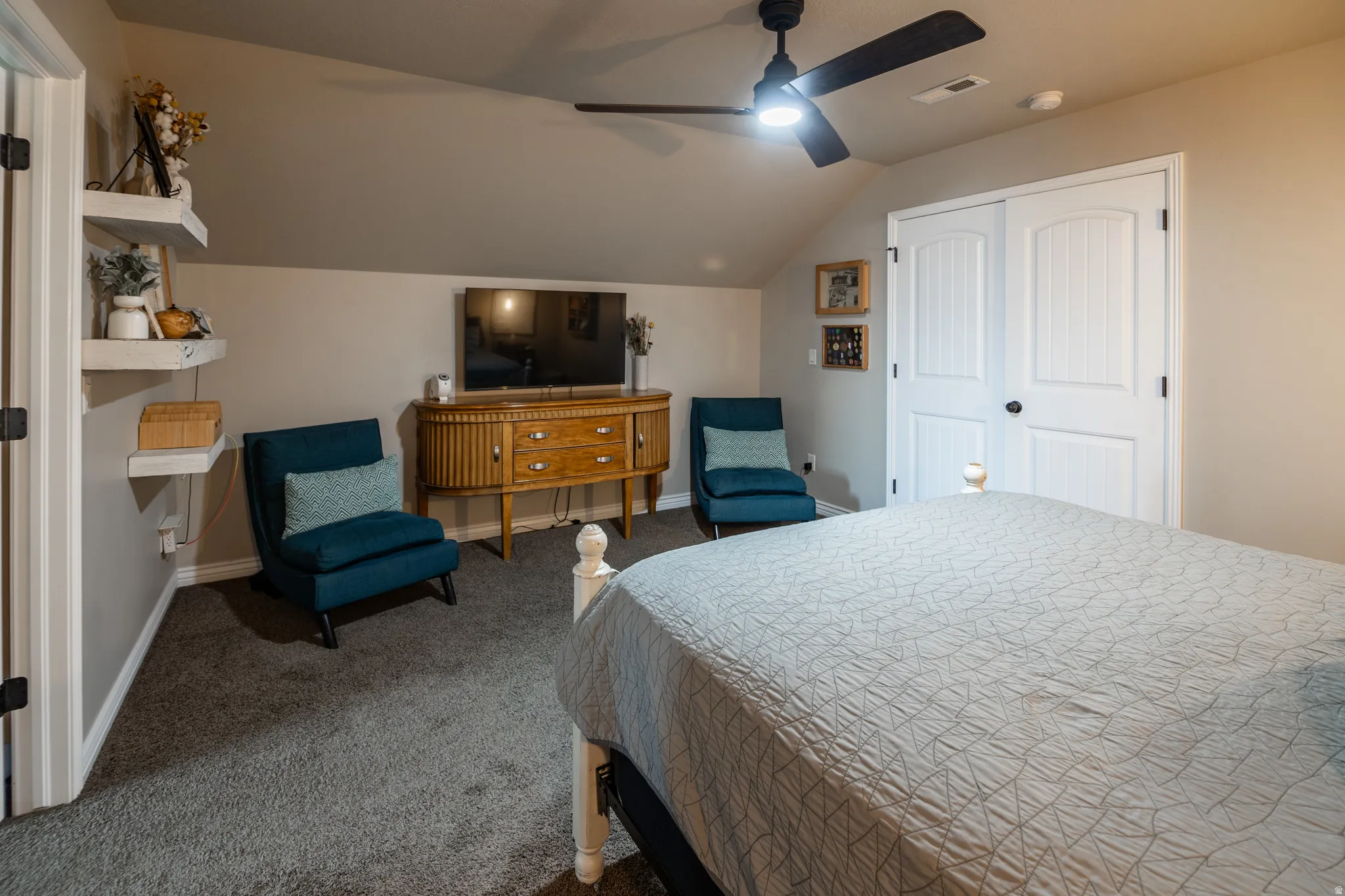 Carpeted room featuring a sloped ceiling, ceiling fan with integrated lighting, built-in shelving, and bifold closet doors
