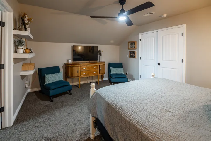 Carpeted room featuring a sloped ceiling, ceiling fan with integrated lighting, built-in shelving, and bifold closet doors