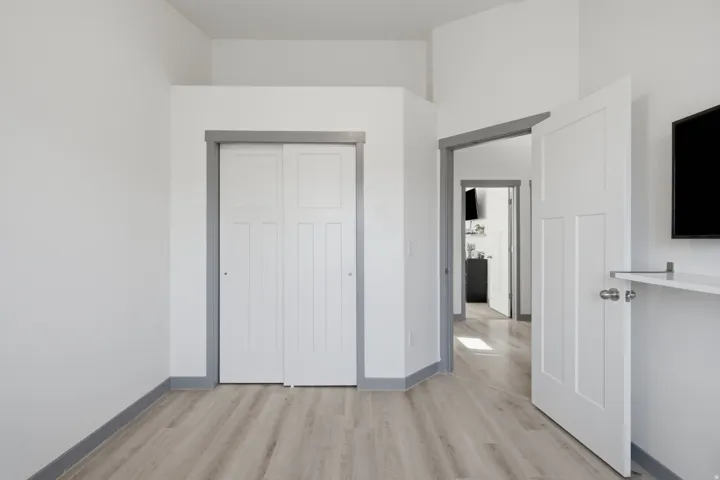 Light-toned wood-finish flooring, white walls, and white interior doors with a two-panel design