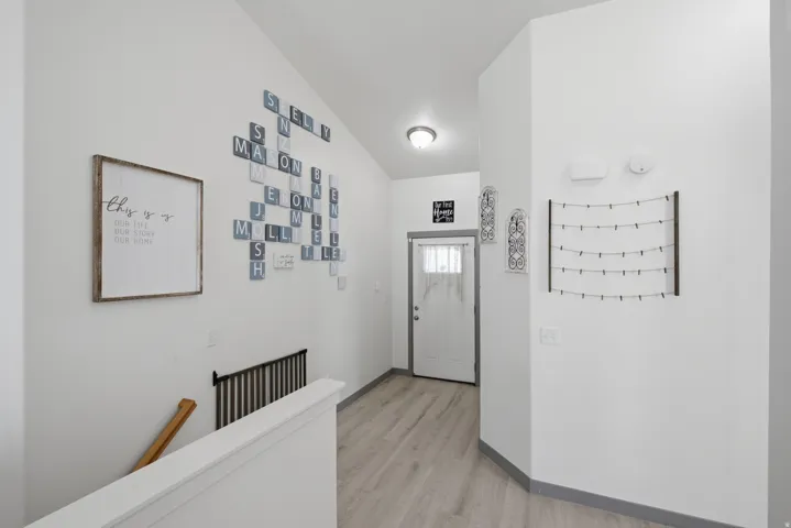 Vaulted ceiling with a flush-mount light fixture, wood-finish flooring, white paneled door with frosted glass, and a white stair railing with dark spindles