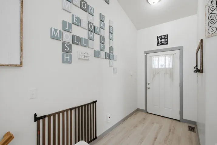 Wood-finish flooring with a white entry door, featuring an overhead light fixture