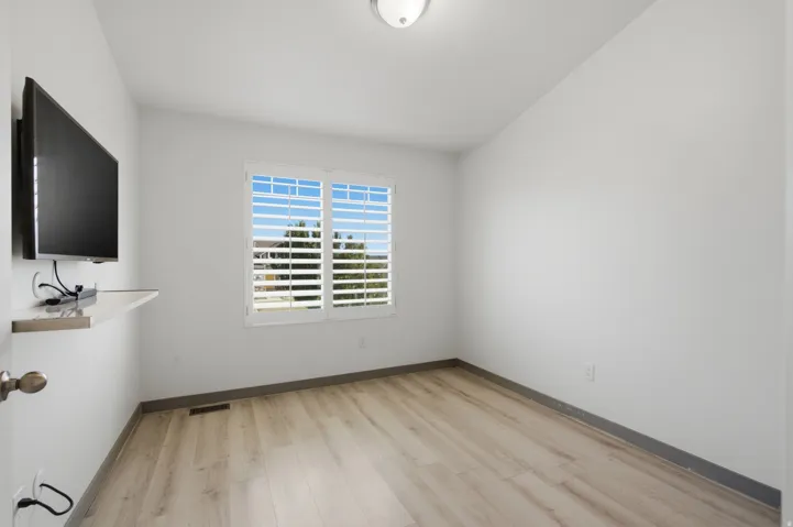 Wood-finish flooring with white walls, window with plantation shutters, and flush mount ceiling light