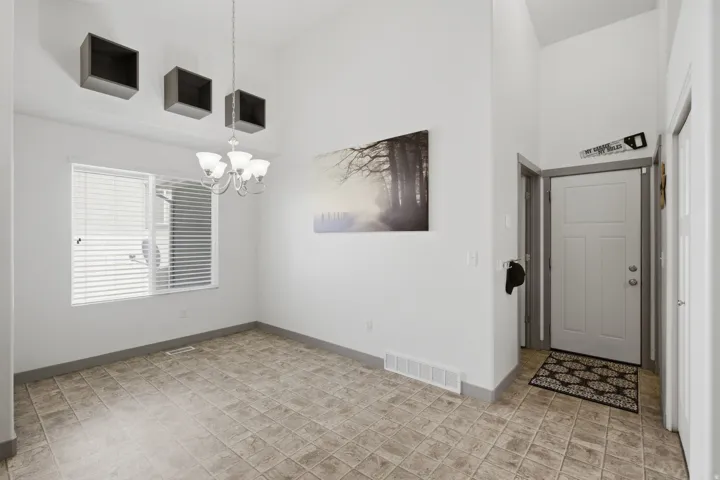 Vaulted ceiling with a hanging chandelier, large window with blinds, tile flooring, and a panel-style door