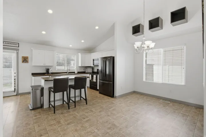 Kitchen island with dark countertops, white cabinetry, integrated black appliances, and vaulted ceilings with recessed lighting