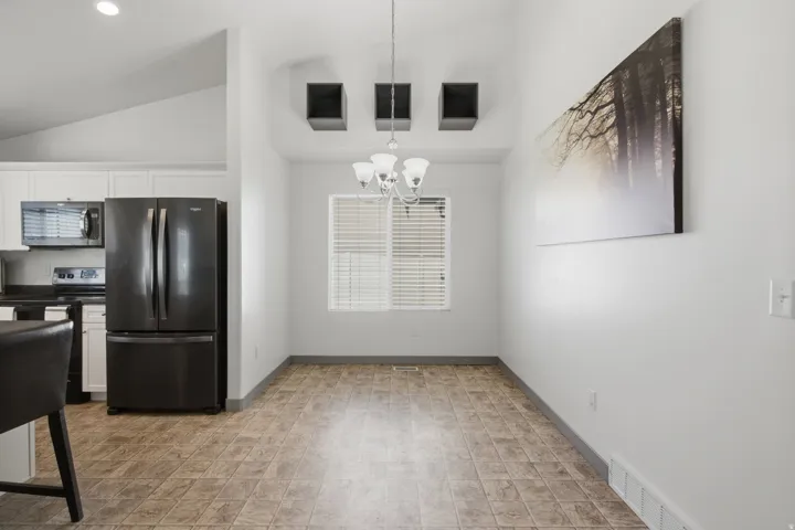 Vaulted ceiling with recessed lighting, pendant chandelier, dark stainless steel refrigerator, and white cabinetry
