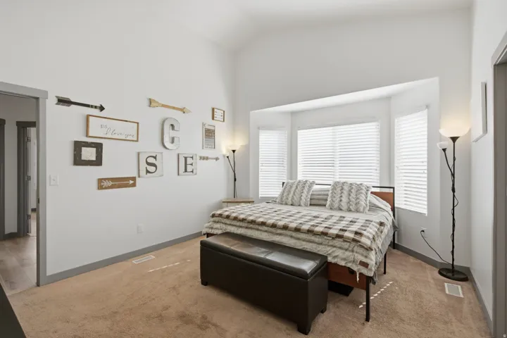 Vaulted ceiling, bay window, white window blinds, light-colored carpeting, and painted trim