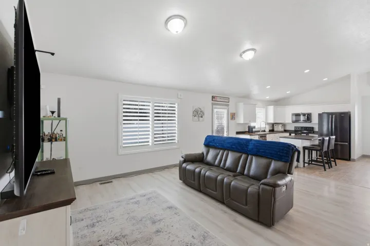 Open-concept living area featuring light wood-finish flooring, white walls, and vaulted ceilings