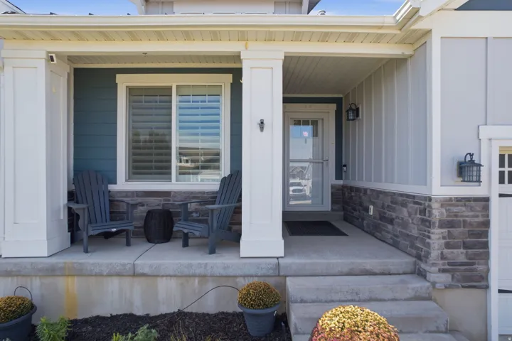 Covered front porch featuring robust columns, stacked stone wainscoting, a panel-style entry door, and vertical plank siding