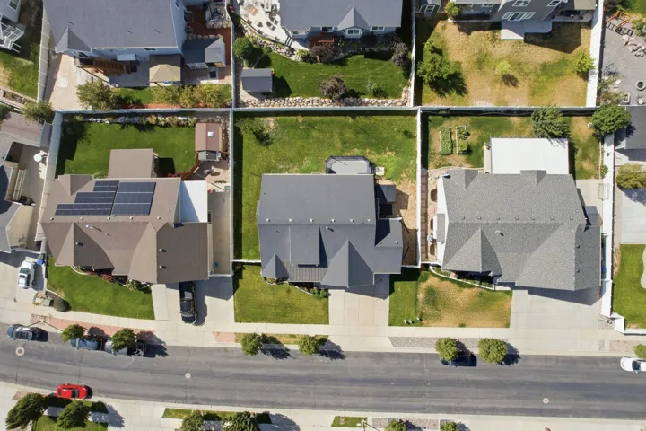 Gabled roofline, solar panel installation, paved driveway, landscaped yard with mature plantings, and perimeter fencing
