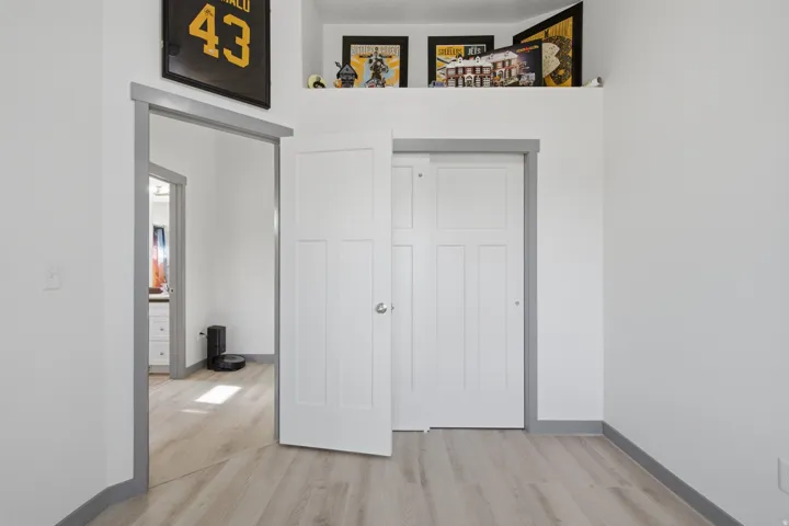 White interior walls with gray trim, wood-finish flooring, and a built-in overhead shelf
