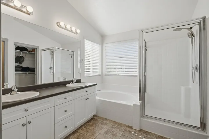 Dual vanity with white cabinetry, built-in bathtub, glass-enclosed shower, and a large mirror