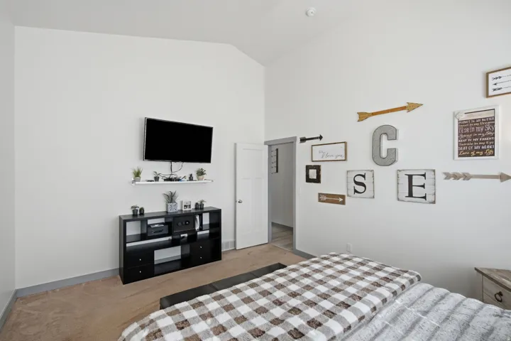 Vaulted ceiling, white walls, and neutral carpet flooring