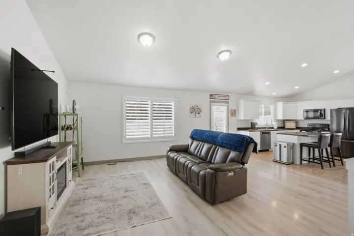 Open-concept living space with light wood-finish flooring, white walls, and a vaulted ceiling