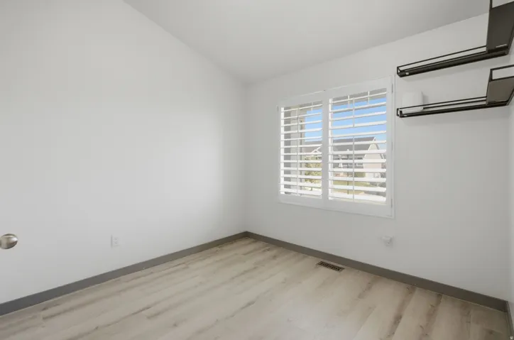 Wood-finish flooring, white walls, and a window with white plantation shutters