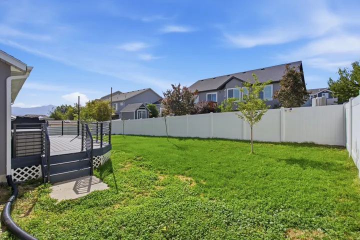 Expansive backyard featuring a manicured lawn, a spacious deck with dark railing, a young tree, and privacy fencing