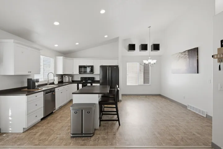 White cabinetry, stainless steel appliances, recessed lighting, vaulted ceiling, and an island with bar seating
