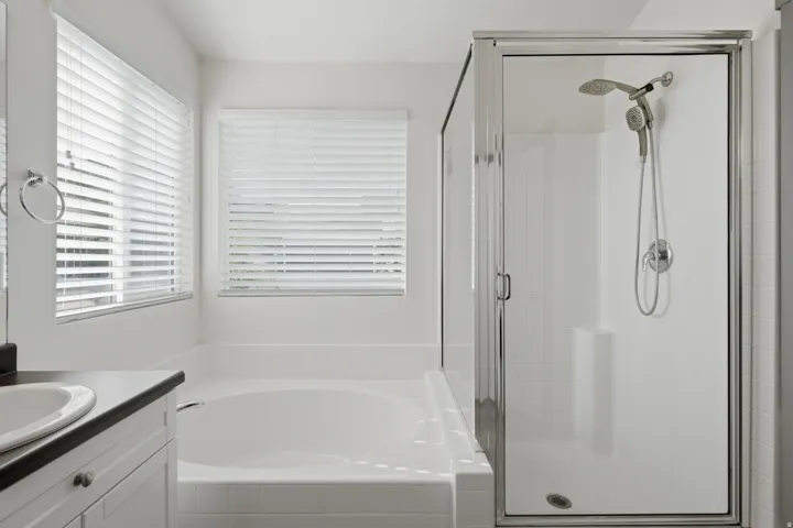 Built-in soaking tub, glass-enclosed shower with tiled walls and built-in bench, dual shower heads, and white cabinetry with an undermount sink