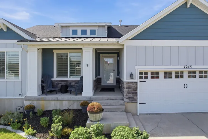 Front exterior with a covered porch, stone accent siding, and a white garage door