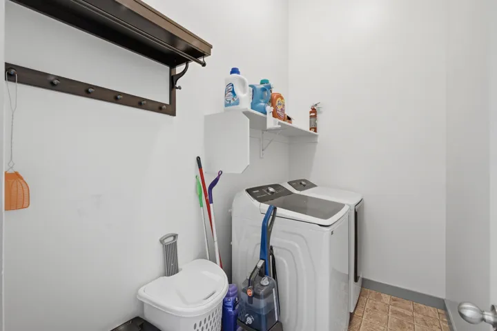 Laundry area featuring a wall-mounted shelf, dark wood-finish coat rack, and tiled flooring