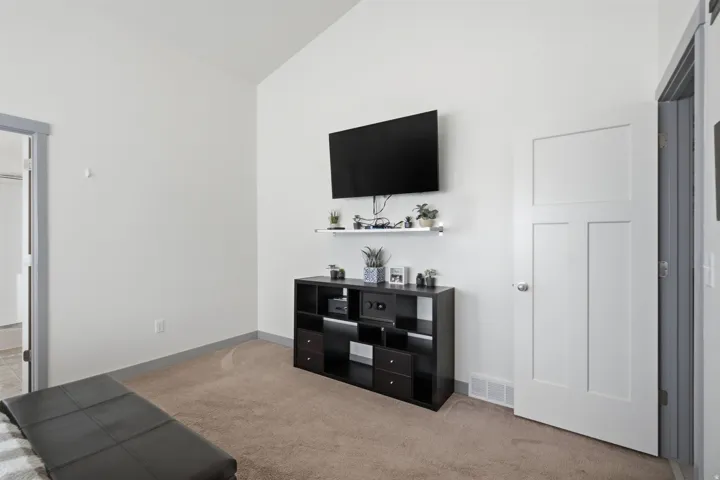 Vaulted ceiling, neutral wall paint, light brown carpet flooring, contemporary white interior door, and grey trim