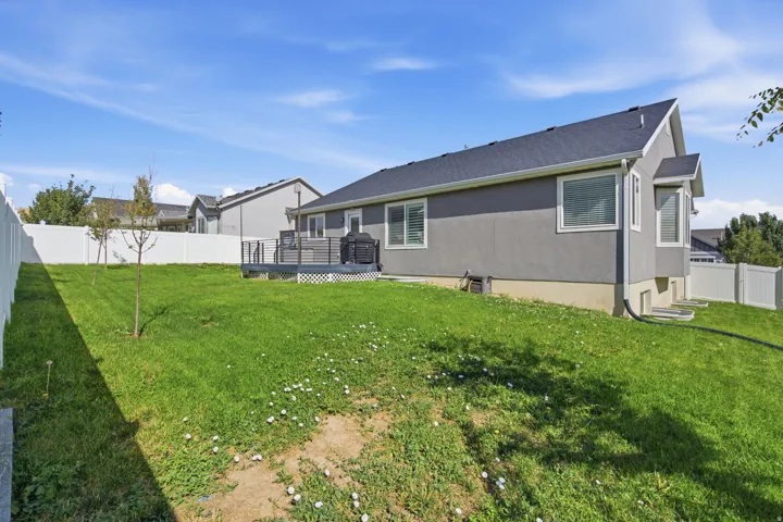 Expansive lawn area with a white privacy fence, multi-level composite deck, and mature trees