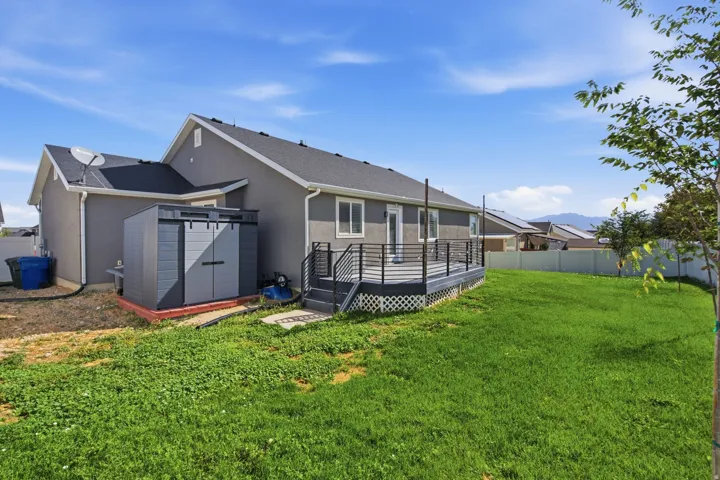 Expansive backyard featuring a manicured lawn, a built-in deck with black railings, and a detached storage shed