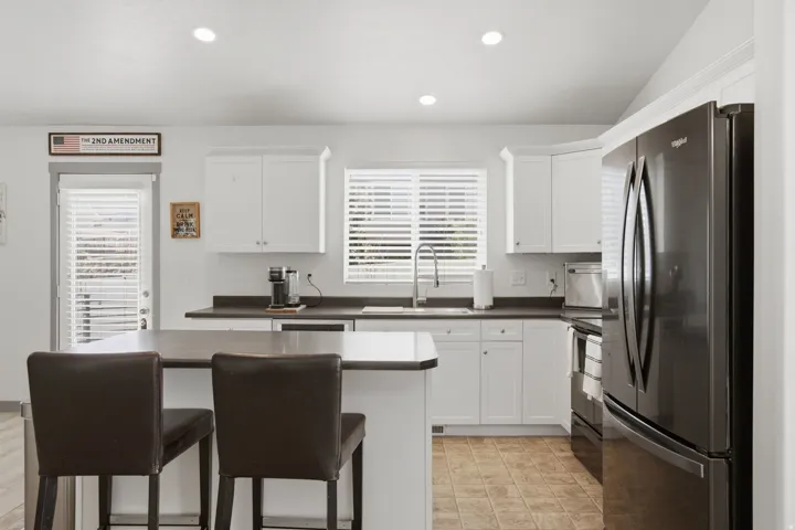 Kitchen featuring white cabinetry, dark countertops, a stainless steel sink, a black refrigerator, and recessed lighting