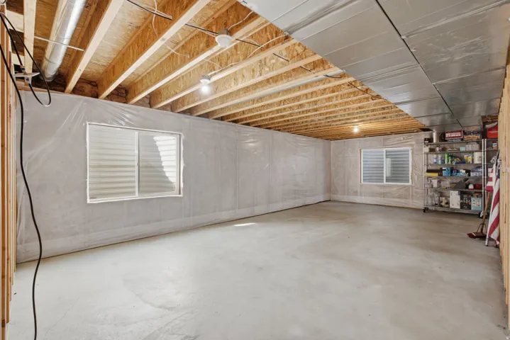 Unfinished basement with concrete flooring, exposed ceiling joists, two basement windows, and unfinished wall studs