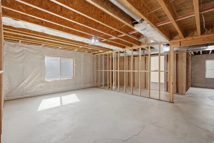 Unfinished basement featuring exposed wood framing, concrete flooring, and an egress window