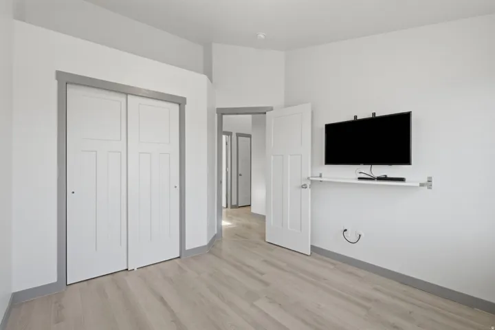 Light wood-finish flooring, white walls, and white interior doors with grey trim