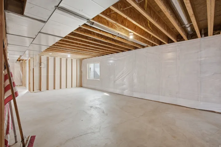 Exposed ceiling joists with partial drop ceiling, concrete flooring, and perimeter wall framing with moisture barrier