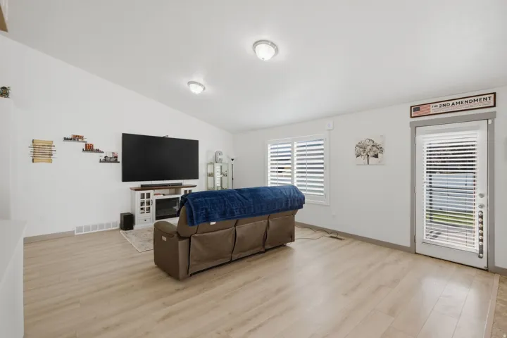 Vaulted ceiling, recessed lighting, wood-finish flooring, white walls, and a glass-paneled door