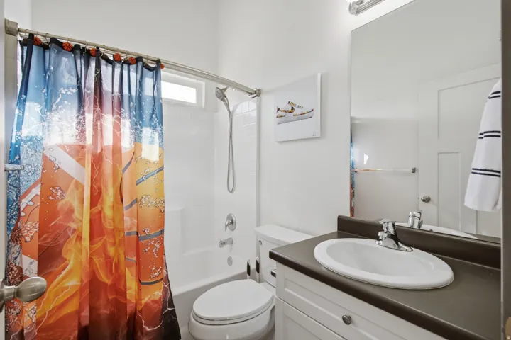 White subway tile shower surround with a built-in tub, white vanity with a dark countertop and integrated sink, chrome fixtures, and a vanity mirror with overhead lighting