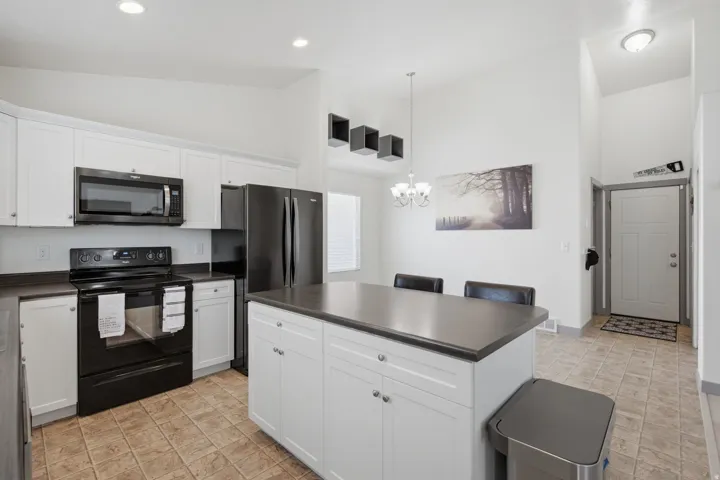 Kitchen featuring white cabinetry, black appliances, a central island with countertop seating, and tiled flooring