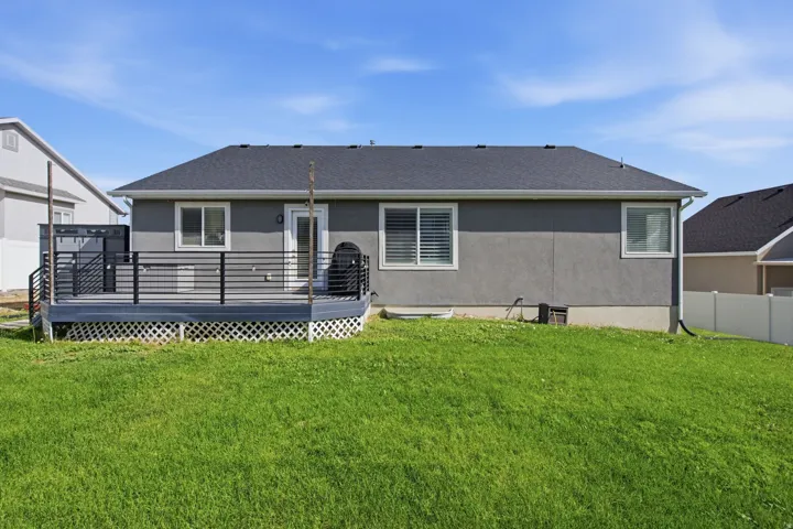 Expansive backyard featuring a manicured lawn, gray stucco exterior, and a dark gray composite deck with black metal railings