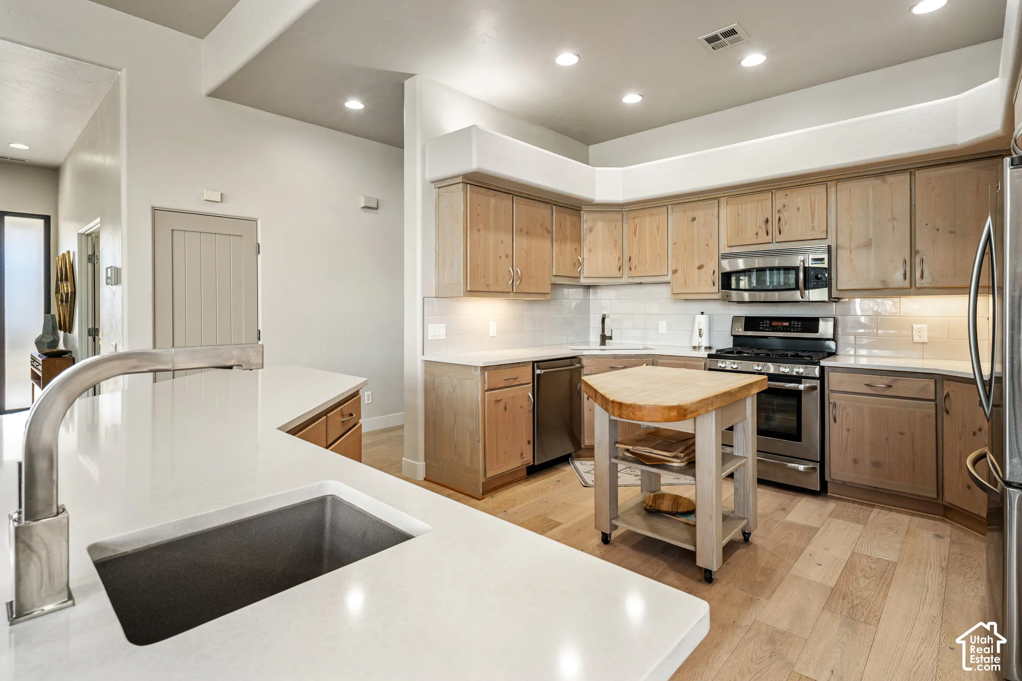 Spacious kitchen featuring light wood-finish cabinetry, stainless steel appliances, white subway tile backsplash, and light-toned countertops