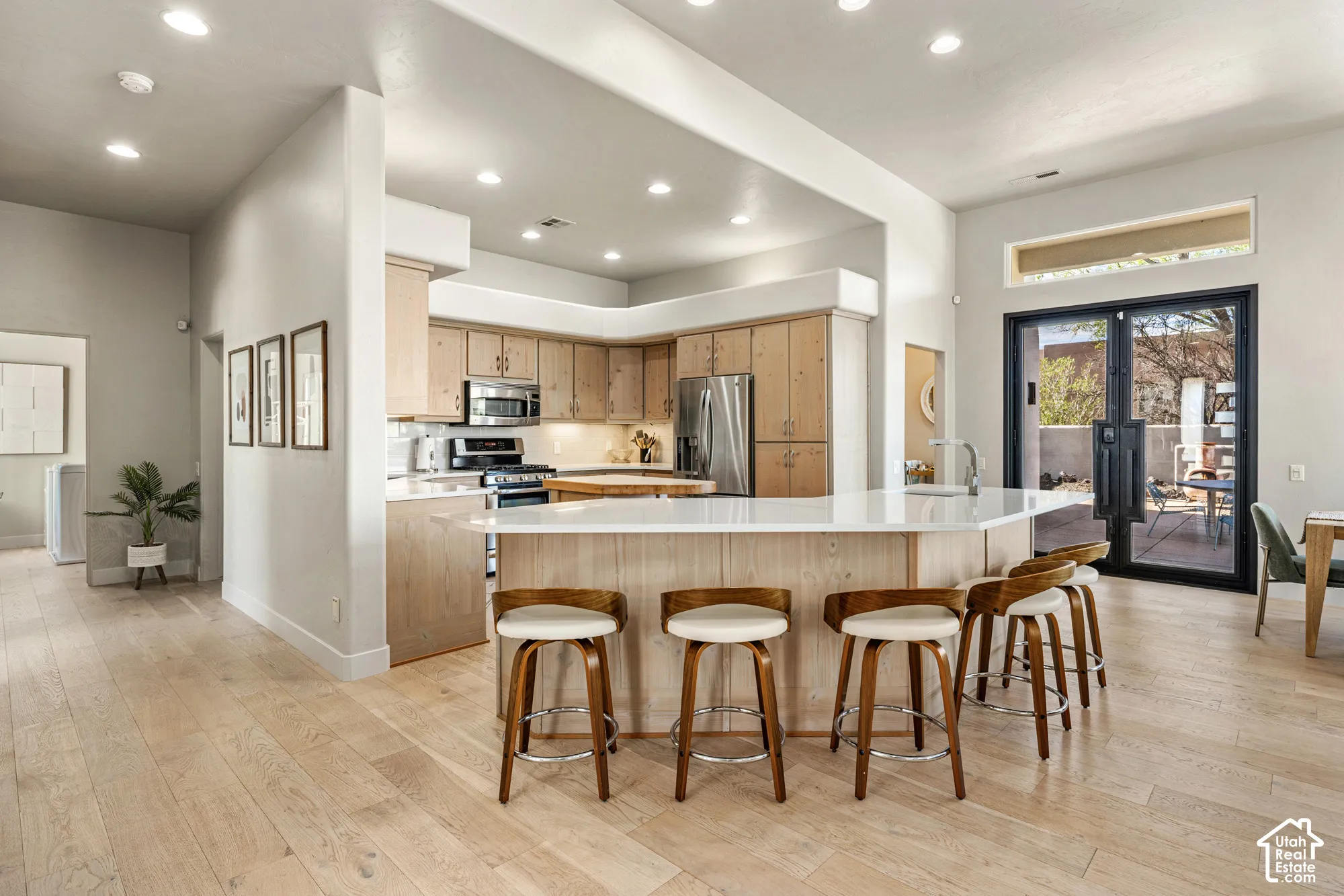 Open-concept kitchen with light wood-finish cabinetry, stainless steel appliances, and a central island with a white countertop
